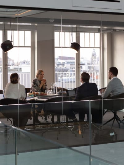 Four people sit in a glass conference room.